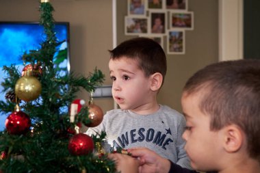 Çocuklar evlerinde aileleriyle Noel ağacı süslüyorlar.