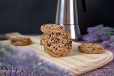 Çikolatalı kurabiyeler, bir bardak süt ve bir sürahi kahveyle ahşap bir masada.