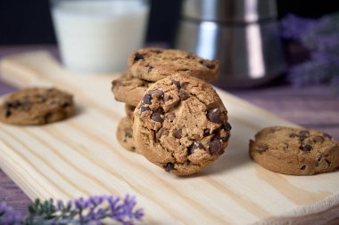 Tahtada bir yığın lezzetli çikolatalı kurabiye, bir bardak süt ve bir fincan kahve.