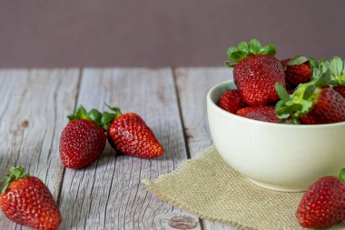 Tahta bir masanın üstünde bir kasede çilek.