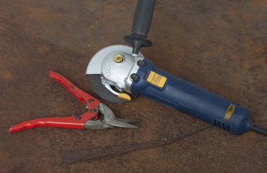 Angle grinder with thinner cut-off disc and red shears for cutting metal on  old rusty metal sheet.  clipart