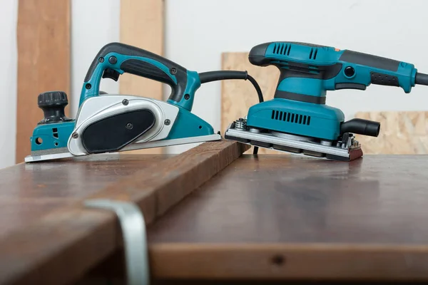 Electric planer and electric sheet finishing sander on wood lath on desk, on background oriented strand board