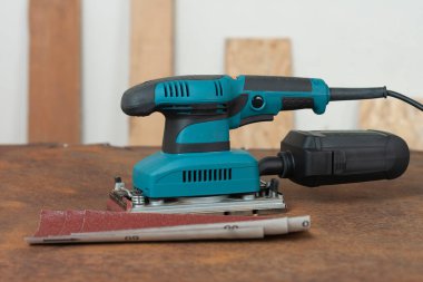 Elektrik levhası zımparalamayı bitiriyor ve arka planda paslı metal levha üzerine üç aşındırıcı kağıt var.