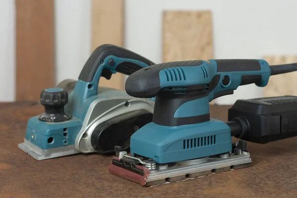 Electric planer and electric sheet finishing sander on old rusty metal sheet, on background oriented strand board