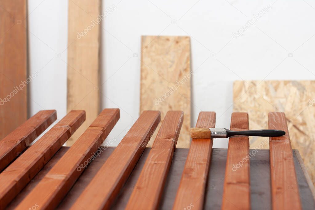 Wooden slats  for production of  wooden garden bench and paintbrush on table in carpentry worksho