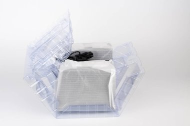 Beyaz arka planda şeffaf plastik poşette iki bilgisayar hoparlörü. Hoparlörlerin ortasında AC adaptörlü kara kutu var..