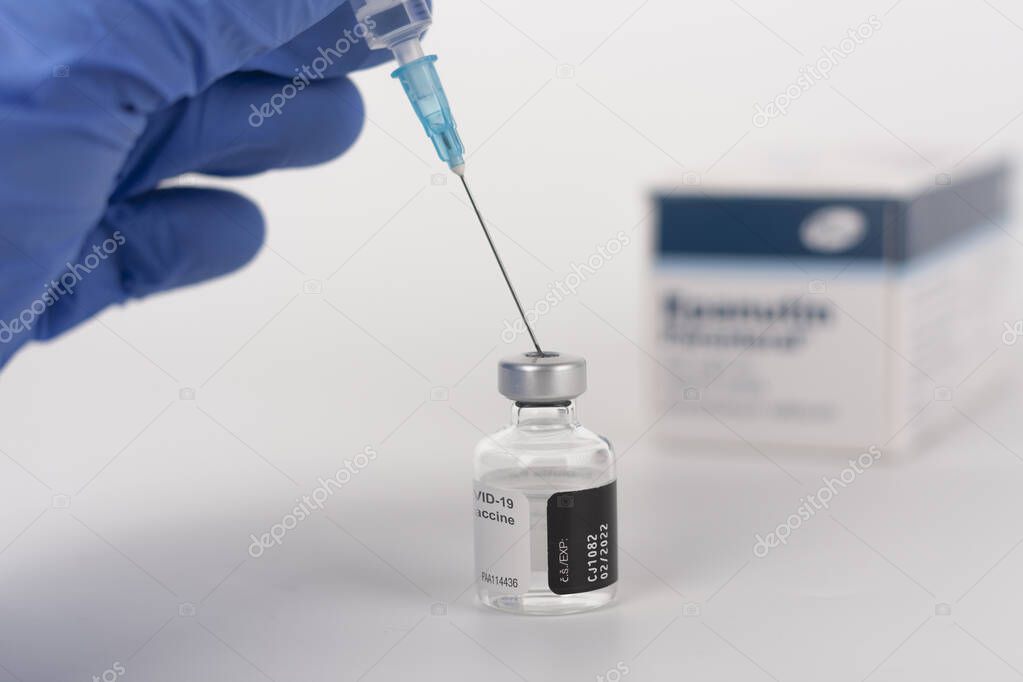 Close up human fingers in gloves, holding syringe with needle and covid-19 vaccine vial. Medical concept.