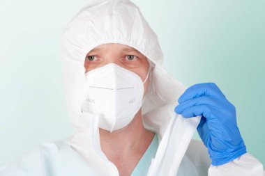 Yüz maskesi ffp2 olan erkek hemşire koruyucu giysilerini çıkartıyor. Hastanedeki yoğun bakımda virüse karşı korunmak için kişisel koruyucu ekipmanlar..