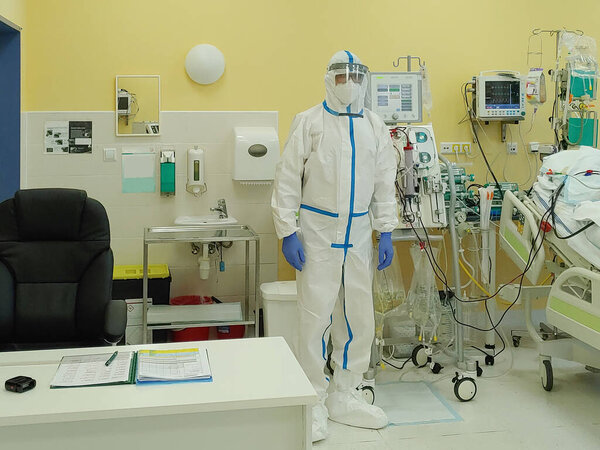 Мужчина медбрат в защитной одежде в отделении интенсивной терапии в больнице. Машина для диализа, к которой подключен пациент. Пациент заболел новым типом коронавируса covid-19. 