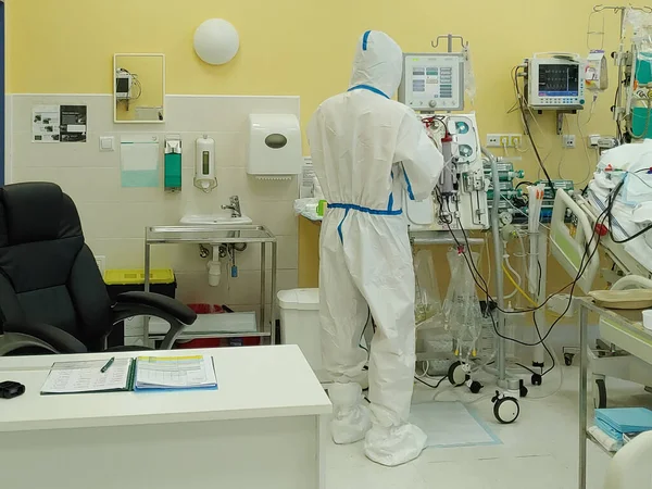 病院の集中治療室で保護カバーの服を持つ男性看護師 患者が接続されている透析装置 患者は新しいタイプのコロナウイルスCovid 19で病気になった ロイヤリティフリーのストック画像
