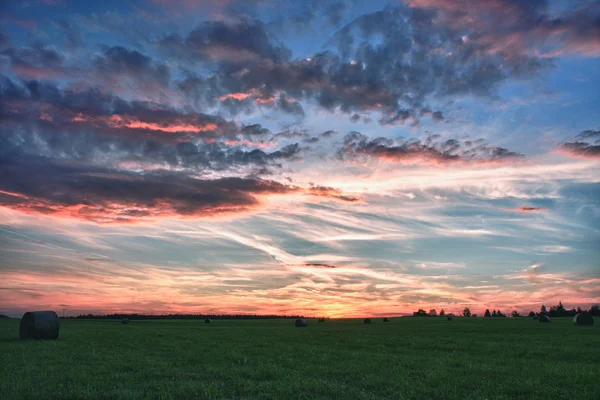 Balíky sena na louce proti krásné nebe s mraky v západu slunce v hdr fotografie — Stock fotografie