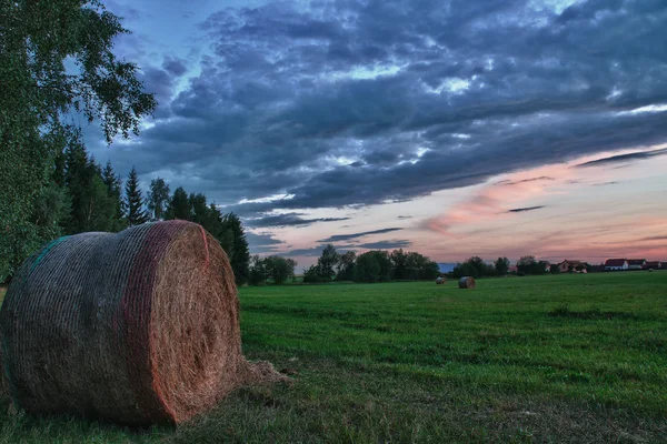 Fardos de feno em um prado contra o céu bonito com nuvens no pôr do sol na foto hdr — Fotografia de Stock