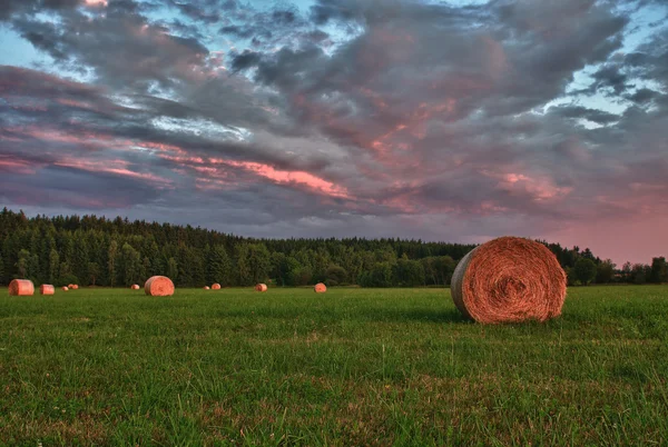 Fardos de feno em um prado contra o céu bonito com nuvens no pôr do sol na foto hdr — Fotografia de Stock