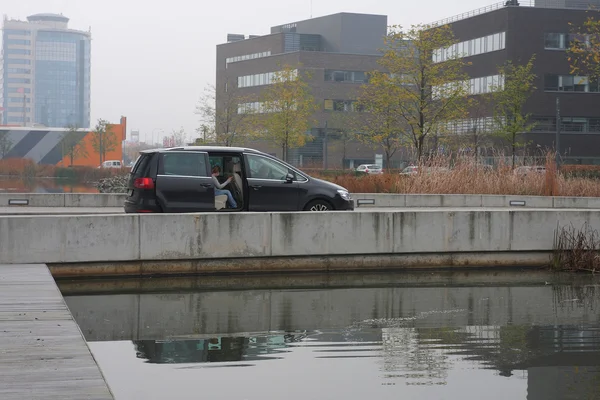 Black car in office centre with park and fish-stocked lake.