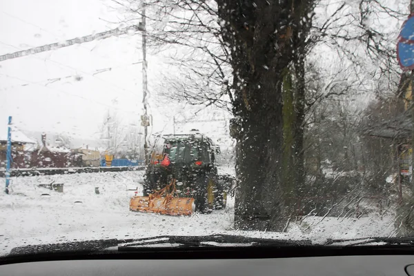 Um trator numa estrada durante uma tempestade de neve — Fotografia de Stock