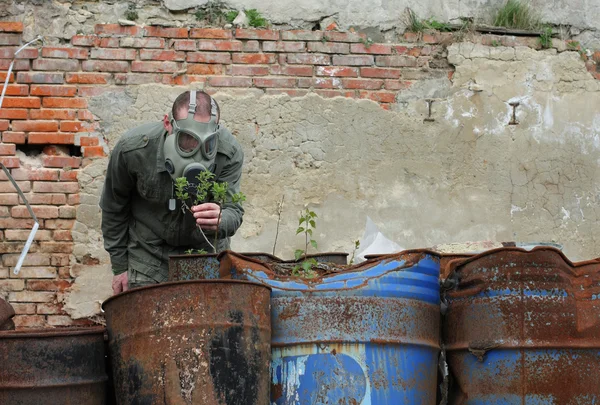 Man met gas masker en groene militaire kleren verkent kleine plant na de ramp met chemische. — Stockfoto
