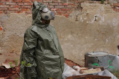 Gaz maskesi ve yeşil askeri giysileri ile adam ölü kuş kimyasal felaketinden sonra araştırıyor.