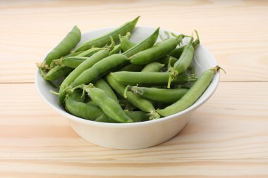 Ahşap masa üzerinde beyaz tabak içinde yeşil bezelye 