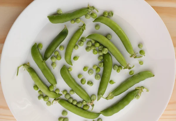 Grüne Erbsen und Erbsenschoten in weißem Teller auf Holztisch — Stockfoto