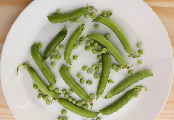 Guisantes verdes y vainas de guisantes en plato blanco sobre mesa de madera — Foto de Stock