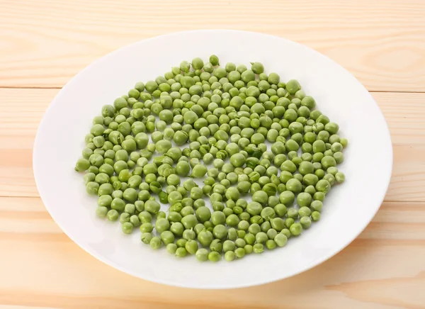 Guisantes verdes en plato blanco y sobre mesa de madera — Foto de Stock