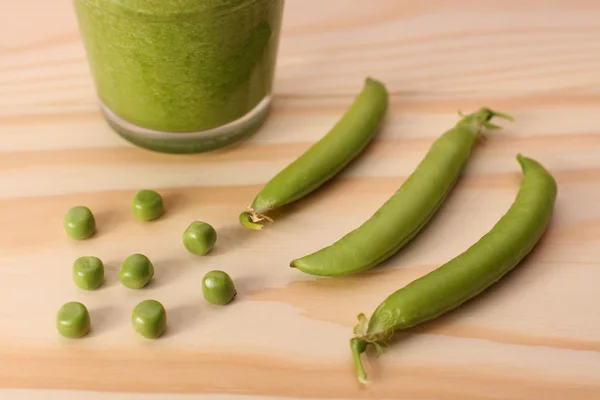 Guisantes verdes y vainas de guisantes y batido verde en mesa de madera — Foto de Stock