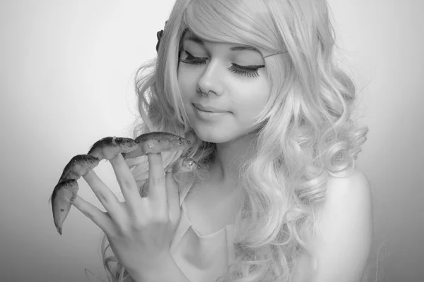 Cara de boneca menina, cabelo encaracolado, com peixe espadilha nos dedos — Fotografia de Stock