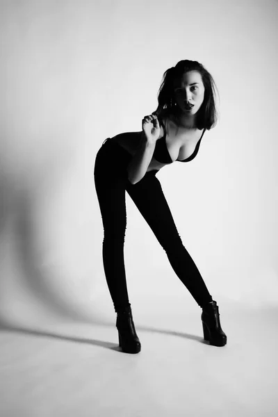 Black and white photo of beautiful brunette woman model  posing in studio. Wearing jeans, bra, heels — Stock Photo, Image