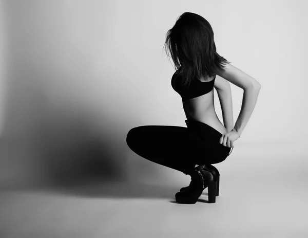 Black and white photo of beautiful brunette woman model  posing in studio. Wearing jeans, bra, heels — Stock Photo, Image