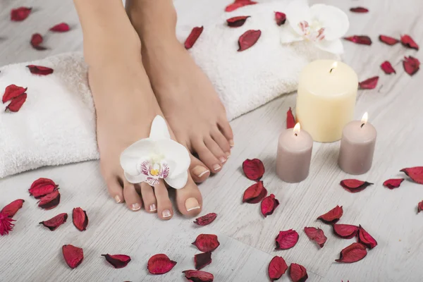 Beautiful female feet and hands with french manicure on white towel. Orchid flowers, red petals, candles around, wooden background. Spa, foot care — Stock Photo, Image