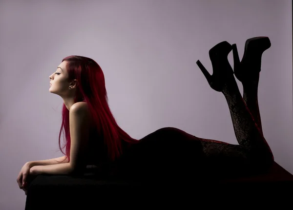 Beautiful red haired woman posing on plinth over grey background — Stock Photo, Image