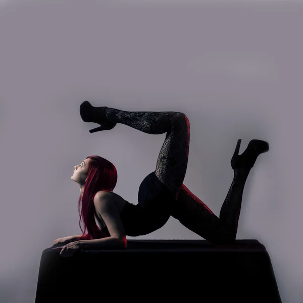 Mooie rode donkerharige vrouw acrobat over grijze achtergrond — Stockfoto