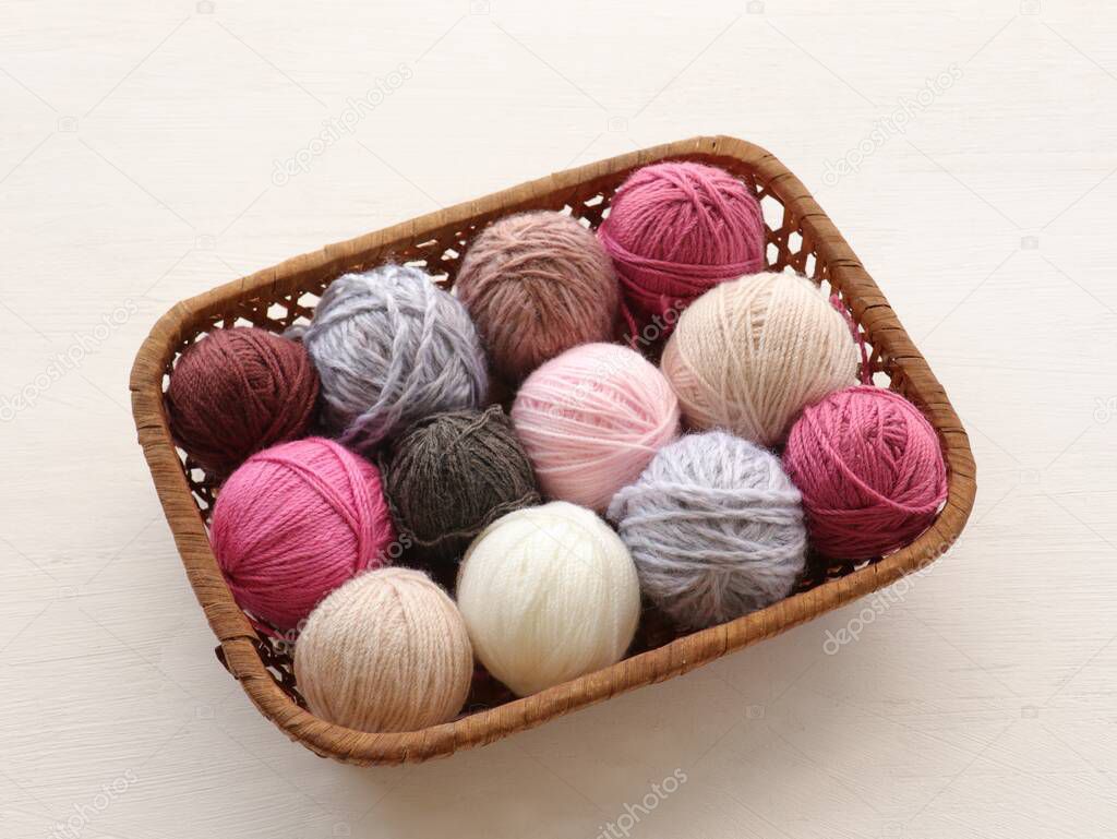 Multicolored knitting yarn balls in basket on white bckground