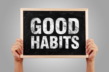Metin iyi alışkanlıklar gri arka plan ile küçük yazı tahtası holding eller.