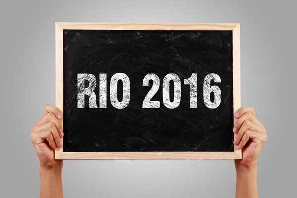 Hands holding small blackboard with text RIO 2016 against gray background.