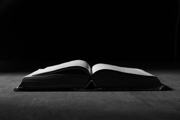 Image of an old holy bible on wooden background in dark.
