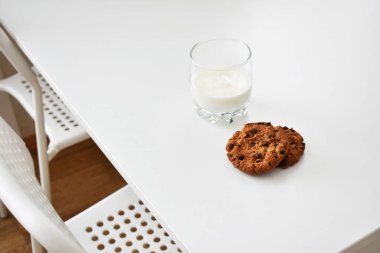 Çikolatalı yulaf ezmeli kurabiye ve beyaz bir masada bir bardak süt..