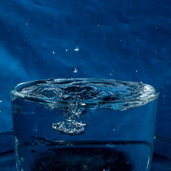 Nyckfull stänk droppar i ett glas vatten Stockbild