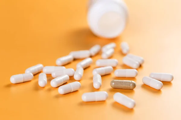 Opposition. A lot of white pills and one brown on a yellow background. The problem of choice and efficiency. Health and medicine.