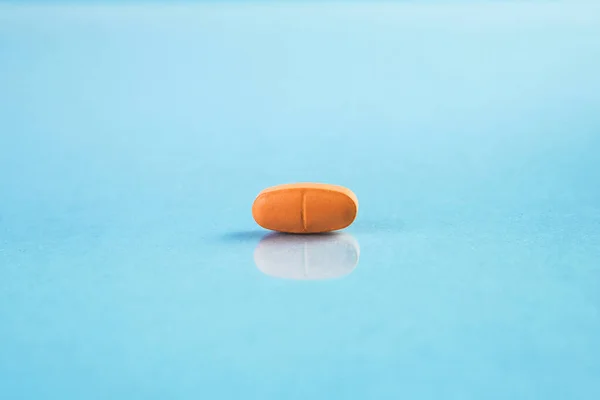 Mavi arka planda turuncu renkli ilaç veya kapsül görüntüsü.