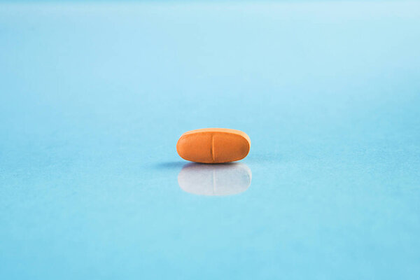 Macro view of orange colored medical pill or capsule on blue background.