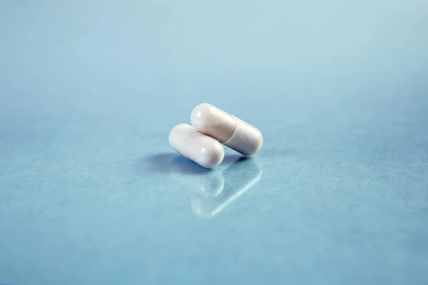 Mavi arka planda iki beyaz kapsül. Reçeteli haplar..