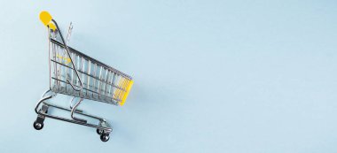 Pastel mavi arka planda sarı, boş bir alışveriş arabası. Alışveriş konsepti.