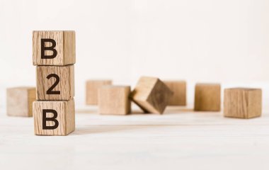 Beyaz masa üzerinde B2B harfleri olan üç tahta küp, daha fazla bulanık küp arka plan.