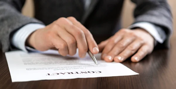 Gri takım elbiseli bir işadamı ofiste kontrat belgelerini okuyor..