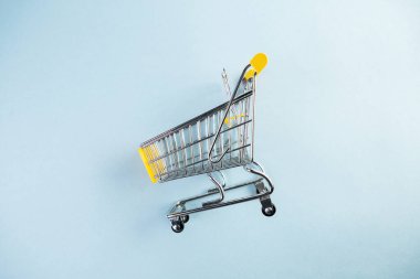 Pastel mavi arka planda sarı, boş bir alışveriş arabası.
