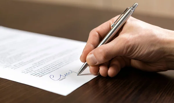 Bir işadamı büro masasında oturup tükenmez kalemle kontrat imzalıyor..