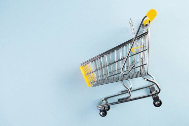 Pastel mavi arka planda sarı, boş bir alışveriş arabası.