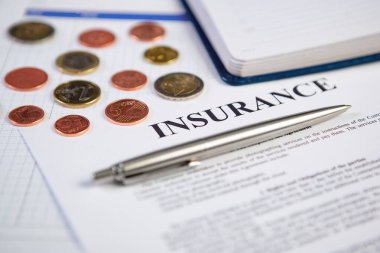 Arkaplanda madeni paralar ve planlama ile sigorta sözleşmesi üzerine gümüş modern kalemi kapatın.