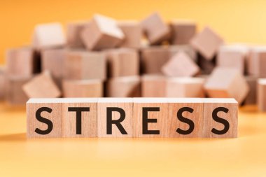 Bulanık küplü sarı arka planda bulunan tahta küplerden oluşan stres kelimesi.